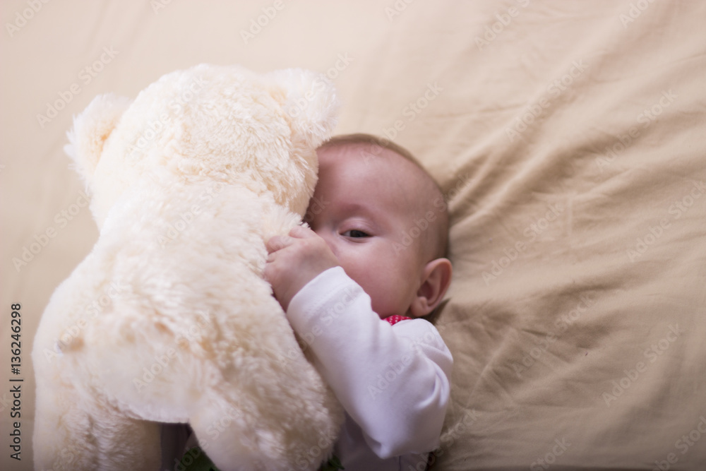 Beautiful baby girl playing with her toys. Close up of a beautiful baby girl lying on the bed. Baby wearing strawberry shirt and pants. Beautiful baby girl playing with her toys. Close up of a beautiful baby girl lying on the bed. Baby wearing strawberry shirt and pants.