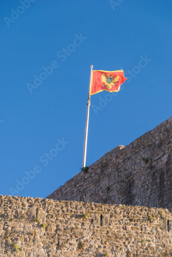 Flag of Montenegro on Budva fortress wall with deep blue sky in the background