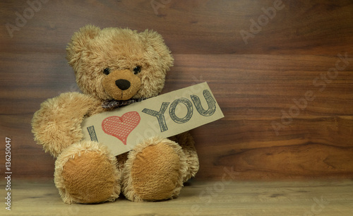 Cute fluffy teddy bear holding a cardboard  I Love You sign, shot on a beautiful wooden surface with enough room for your message