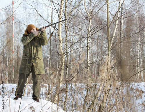 Hunter man with old 16 caliber side-by-side double-barreled shotgun dressed in camouflage clothing in the winter forest