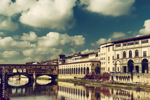 View from the river to the famous italian medieval bridge - Ponte Vecchio in Florence with blue sky and clouds, travel outdoor Italy sightseeing background