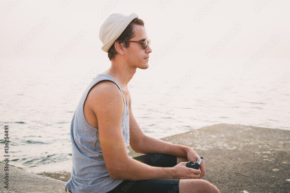 Young hipster man sitting and vaping on sea front Young hipster man sitting and vaping on sea front