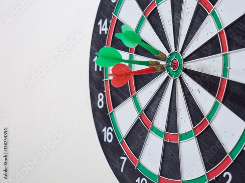 Red and green dart arrow hitting on center target of dartboard.