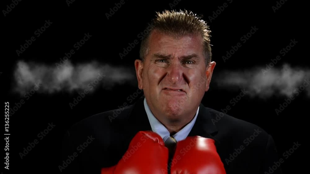 An angry, middle-aged businessman wearing boxing gloves shoots steam from his ears as he becomes more irritated.. An angry, middle-aged businessman wearing boxing gloves shoots steam from his ears as he becomes more irritated..
