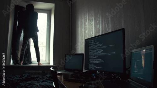 Young in dark hood standing on the windowsill and covering windows with black curtain photo