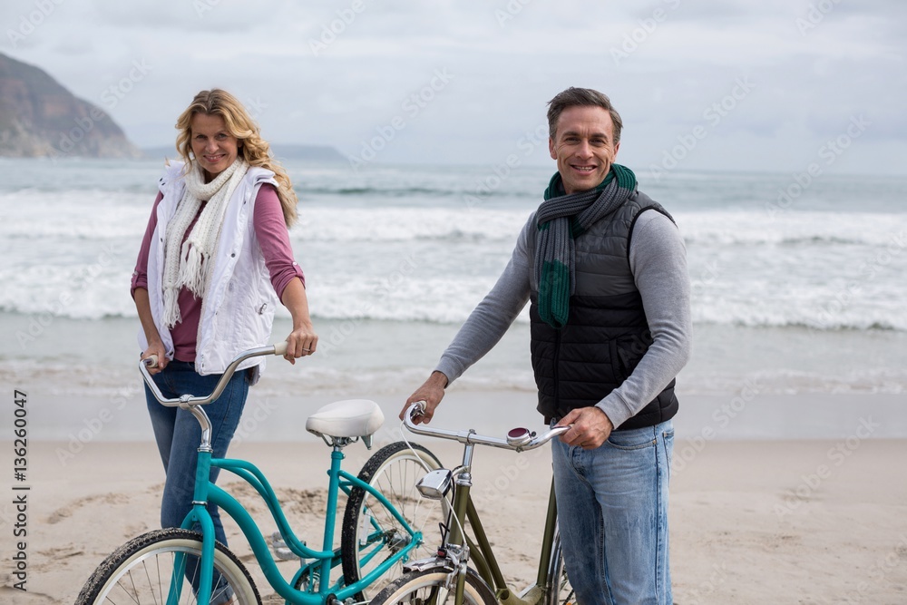 Mature couple standing with bicycles on the beach 