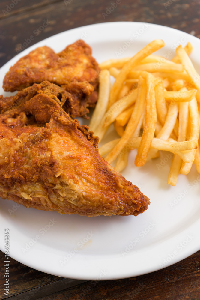 Fried chicken breast with potato chips on a white plate on a wooden table. Fried chicken breast with potato chips on a white plate on a wooden table.