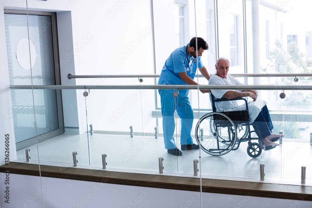 Male doctor pushing senior patient on wheelchair in passageway Male doctor pushing senior patient on wheelchair in passageway