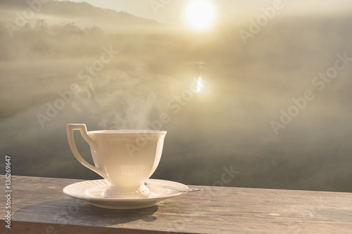 Morning cup of coffee with mist over lake at sunrise
