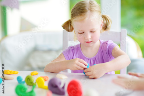 Cute little girl having fun with modeling clay at a daycare. Creative kid molding at home.