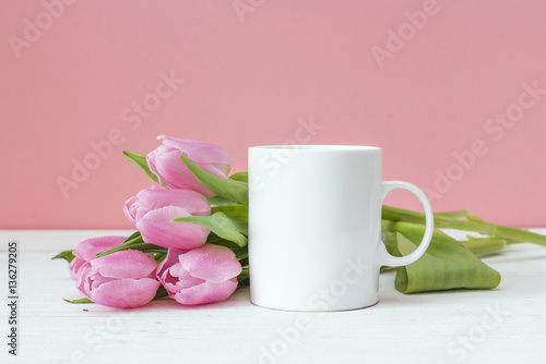 White coffee mug with pink tulips on a pink background. Space fo