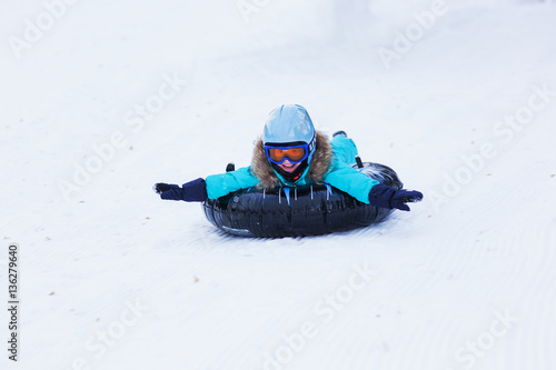Schilderij op canvas cheerful girl in a helmet and glasses riding on a sled with high mountains