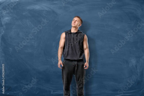 Muscular young man is standing and looking up on blue chalkboard background