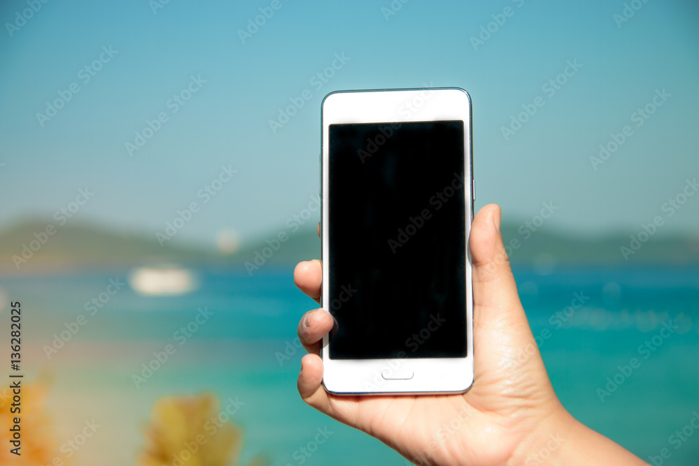 hand hold smart phone on blurred beautiful sea blue sky with pal