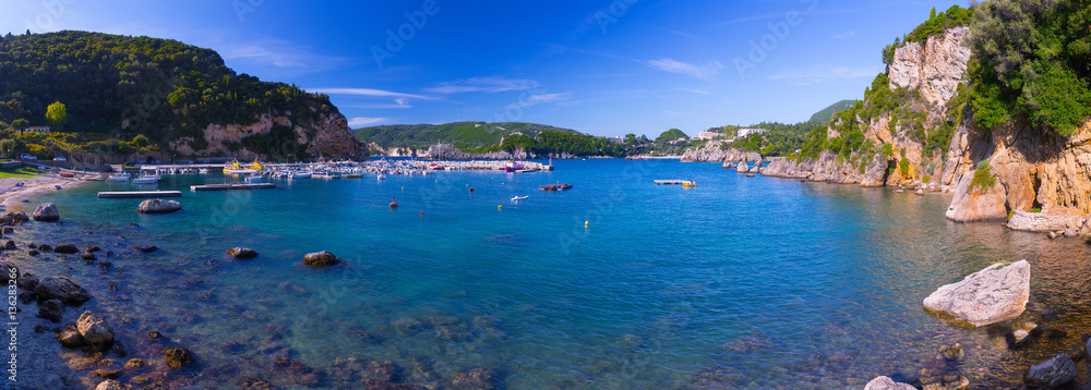 Beautiful summer panoramic seascape. View of the cliff into the sea bay with crystal clear azure water. Boats and yachts moored in the harbor. Paleokastrica. Corfu. Ionian archipelago. Greece.
