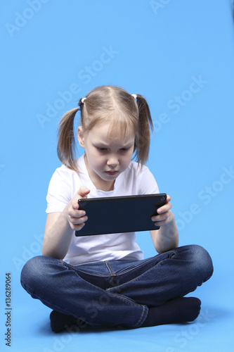 girl sits and plays on the tablet. isolated on blue background