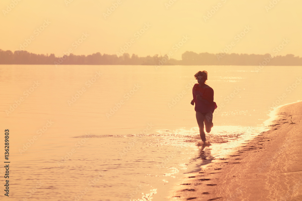 Naklejka premium Teen girl running on the water at sunset