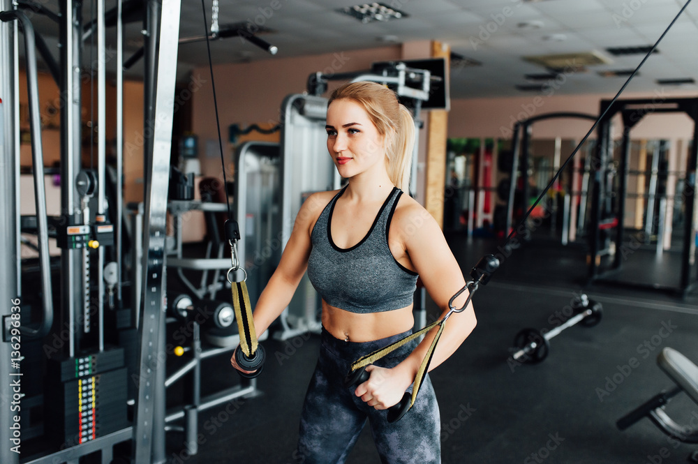 Athletic young woman doing exercises on the simulator for the upper muscle groups Athletic young woman doing exercises on the simulator for the upper muscle groups
