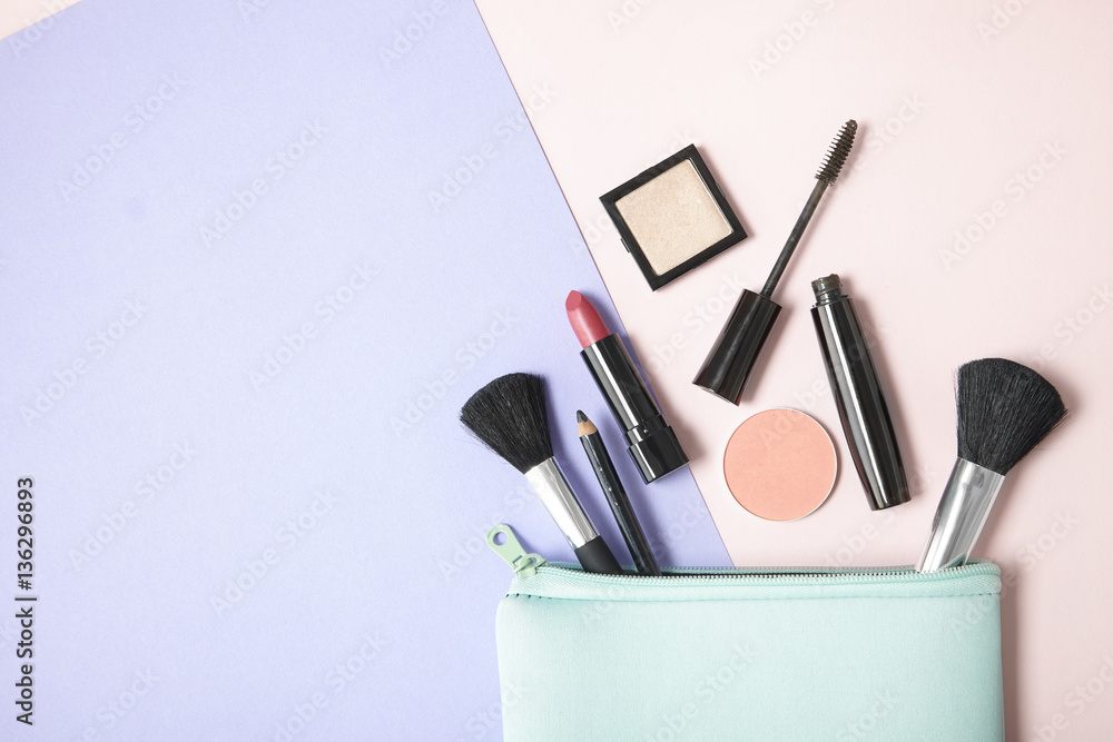 Make up products spilling out of a pastel blue cosmetics bag, on a pink and purple background with blank space at side - obrazy, fototapety, plakaty 