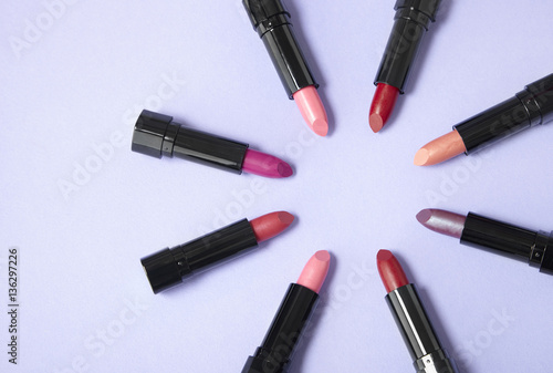 Lipstick make up arranged in a circle on a pastel purple background with blank space at side