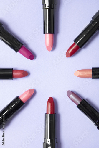 Lipstick make up arranged in a circle on a pastel purple background, forming a page border