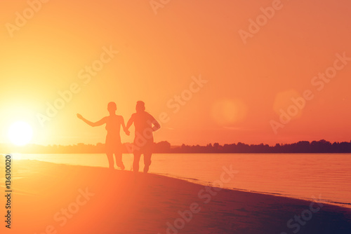 Naked man and a woman running on the beach at sunset