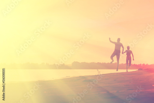 Naked man and a woman running on the beach at sunset