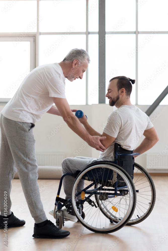 Cheerful disabled man exercising with his coach in the gym Cheerful disabled man exercising with his coach in the gym