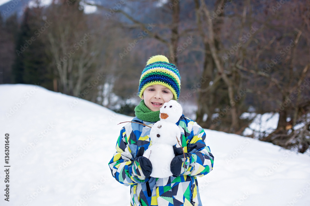 Cute child, building snowman and playing with it on top of mount