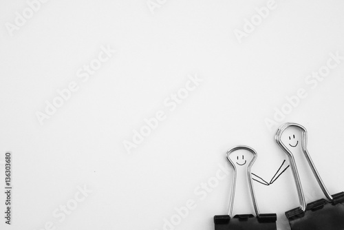 Black paperclip with people holiding hands with smile face on white paper. Love couple concept