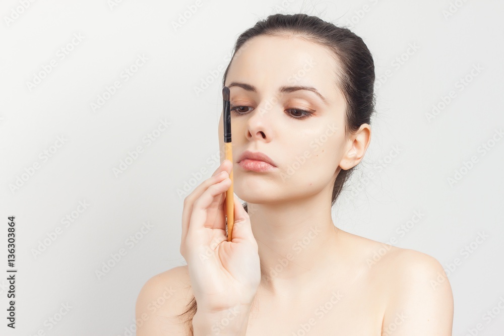 A woman holding a makeup brush in front of her face A woman holding a makeup brush in front of her face