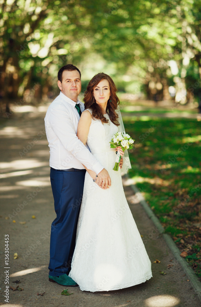 The groom and bride with bouquet stands in the park