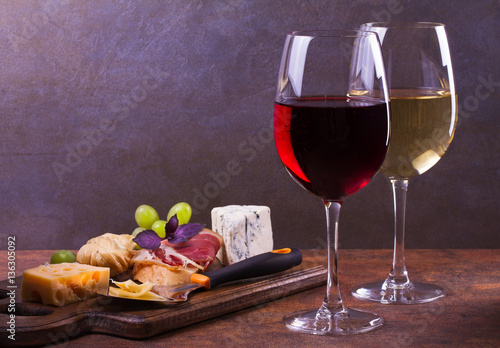 Glasses of red and white wine with smoked cheese, grape, prosciutto, garlic and bread. Wine and cheese still life. Food and drinks concept