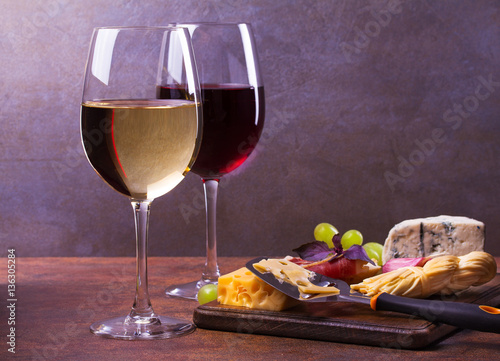 Glasses of red and white wine with smoked cheese, grape, prosciutto, garlic and bread. Wine and cheese still life. Food and drinks concept