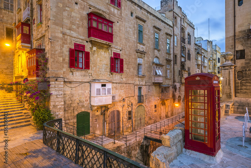 Fototapeta Naklejka Na Ścianę i Meble -  Valletta, Malta - Red vintage british telephone box and footbridge and traditional red balconies in the ancient city of Valletta early in the morning