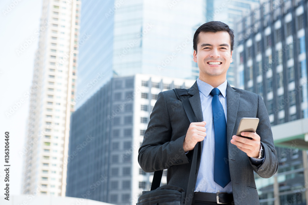 Smiling businessman using mobile phone while carrying bag in the city Smiling businessman using mobile phone while carrying bag in the city