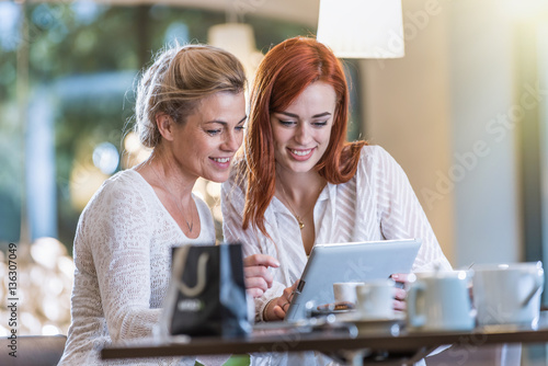  a mother and her daughter sit in a cafe using a tablet