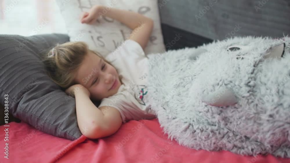 Cute little yawning girl in pajamas lying in a bed under a white blanket on sunny morning Cute little yawning girl in pajamas lying in a bed under a white blanket on sunny morning