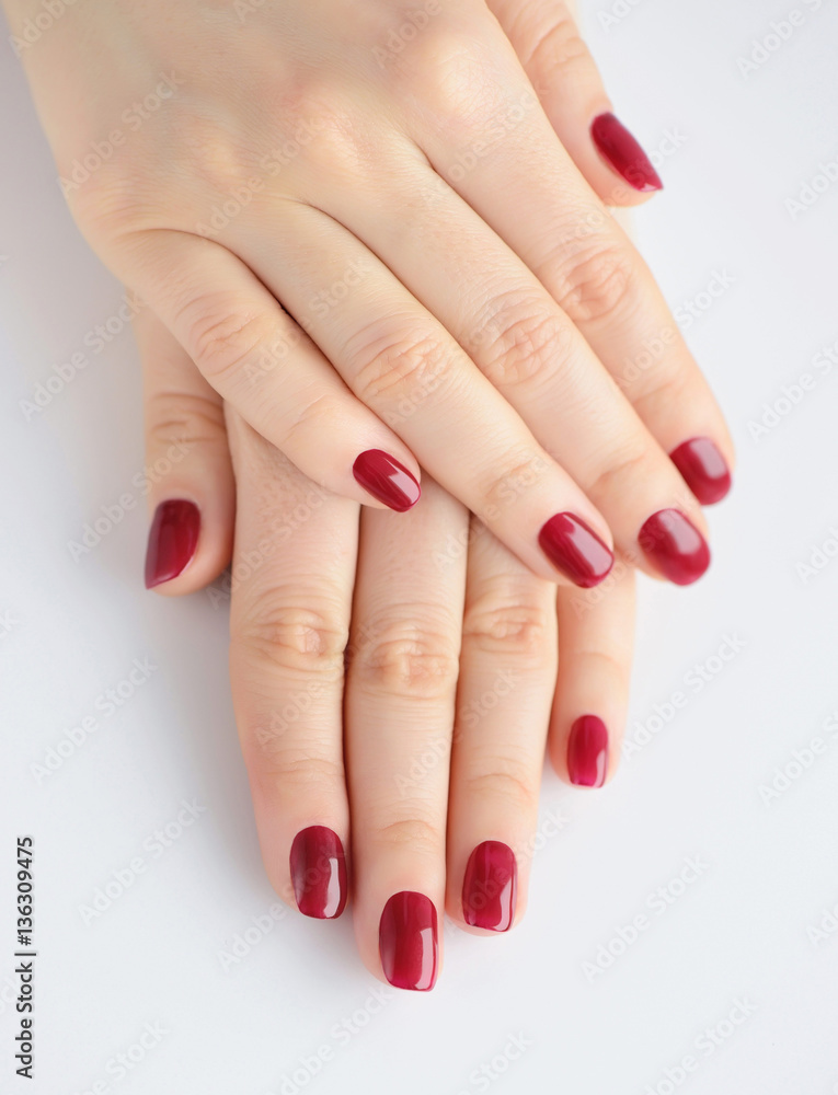 Closeup of hands of a young woman with red manicure on nails against white background Closeup of hands of a young woman with red manicure on nails against white background