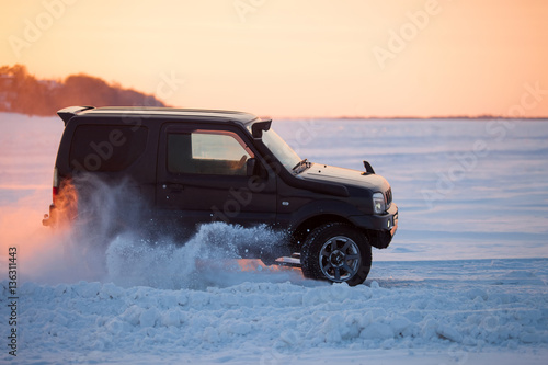 Fotografie Suzuki Jimny moving on ice of a frosn river at sunset