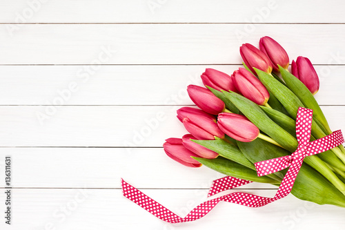 Fototapeta Naklejka Na Ścianę i Meble -  Red tulips bouquet decorated with ribbon on white wooden background. Copy space, top view