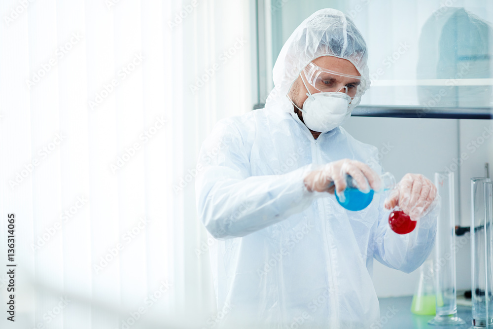 Researcher in protective clothes mixing two liquid substances in lab Researcher in protective clothes mixing two liquid substances in lab