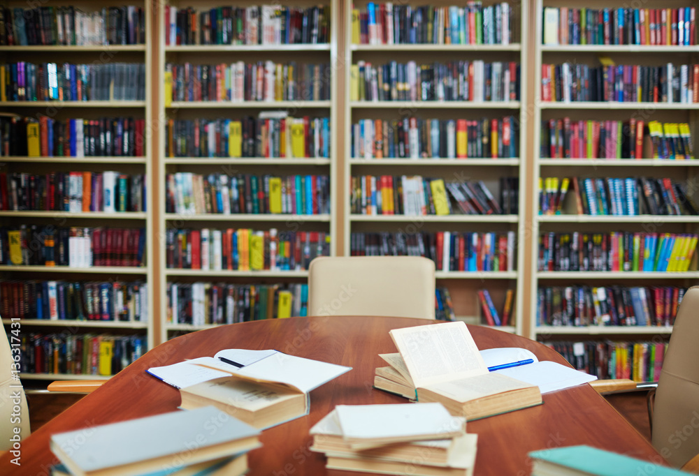 Empty library with bookshelves, desk, some open books and copybooks Empty library with bookshelves, desk, some open books and copybooks
