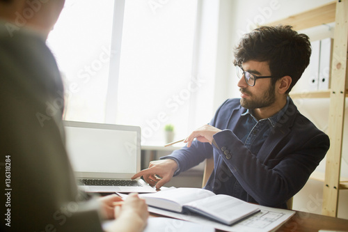 Business people at meeting: young businessman wearing creative haircut and glasses pointing at blank laptop screen
