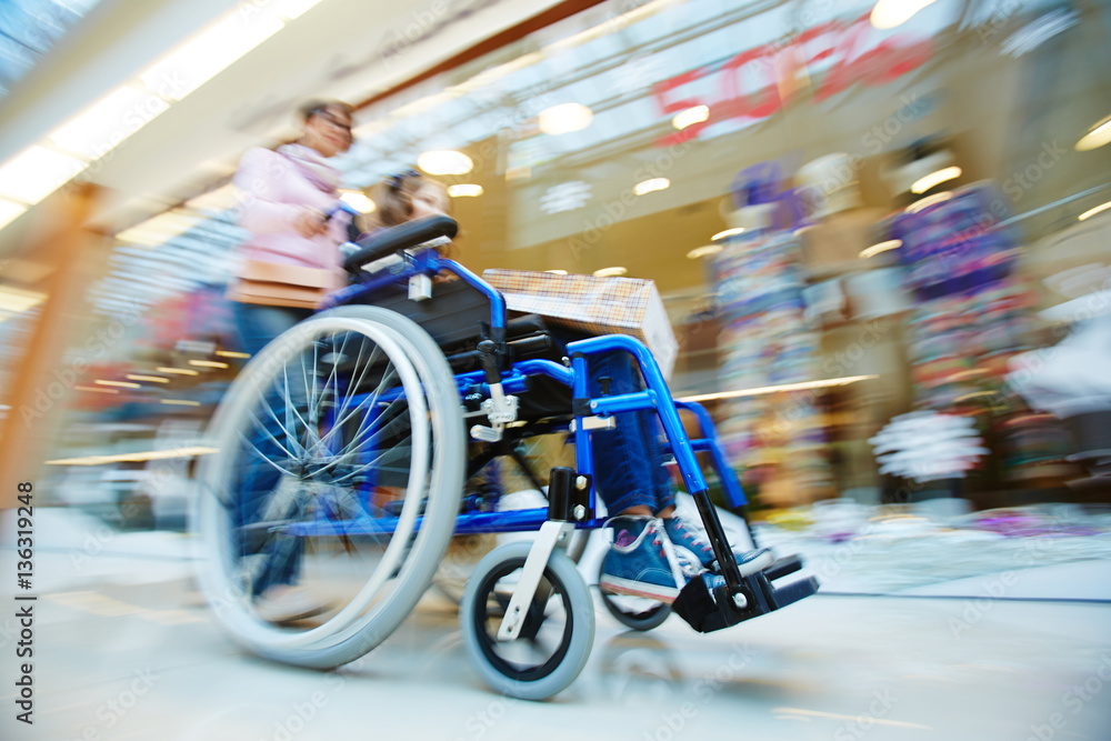 Woman pushing wheelchair with her daughter in the mall Woman pushing wheelchair with her daughter in the mall