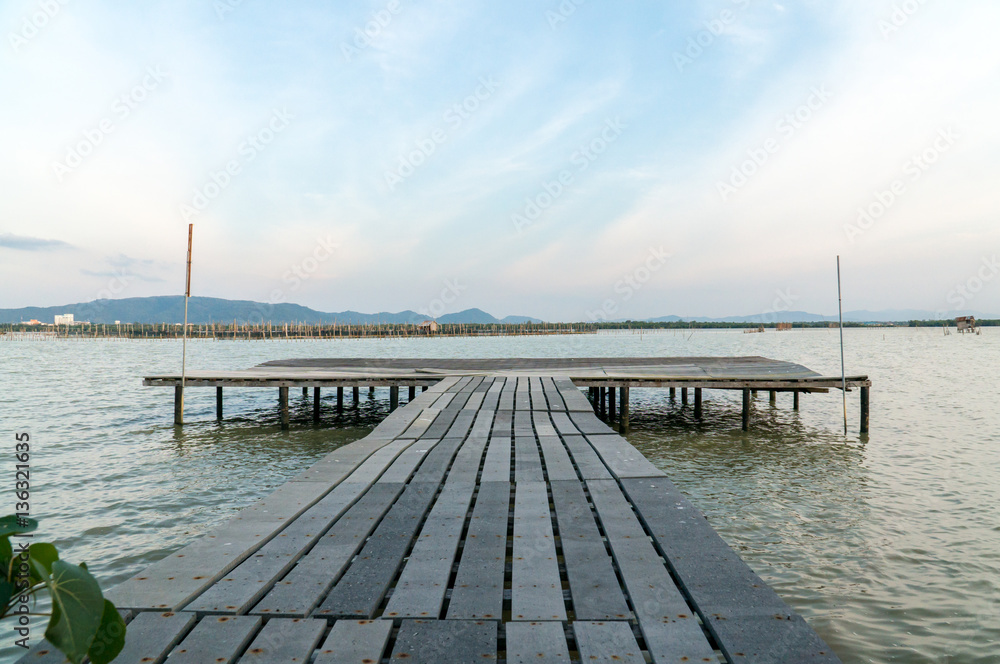 Small wooden pier in the lake with blue sky and mountain in background.