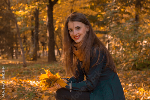 beautiful girl with long hair and red lipstick sits in the Park among the leaves  smiles