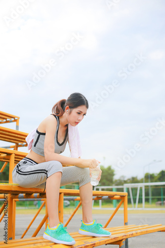 Young woman wearing sports clothes and towels, sport women holding a water bottle and listening to music with headphones © noombluesman