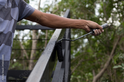 Hand holding paint roller applying black paint on metal stair © bignai