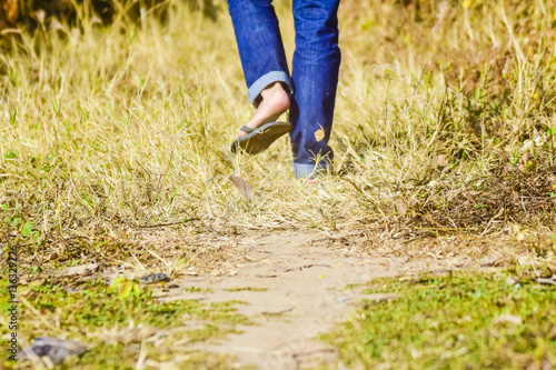 Man wear blue jeans and slippers walk through the dry grass field 